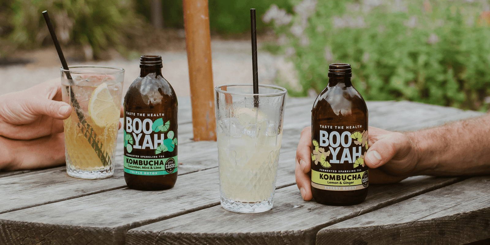 Two bottles of BOOYAH Kombucha on a wooden table with glasses of kombucha.