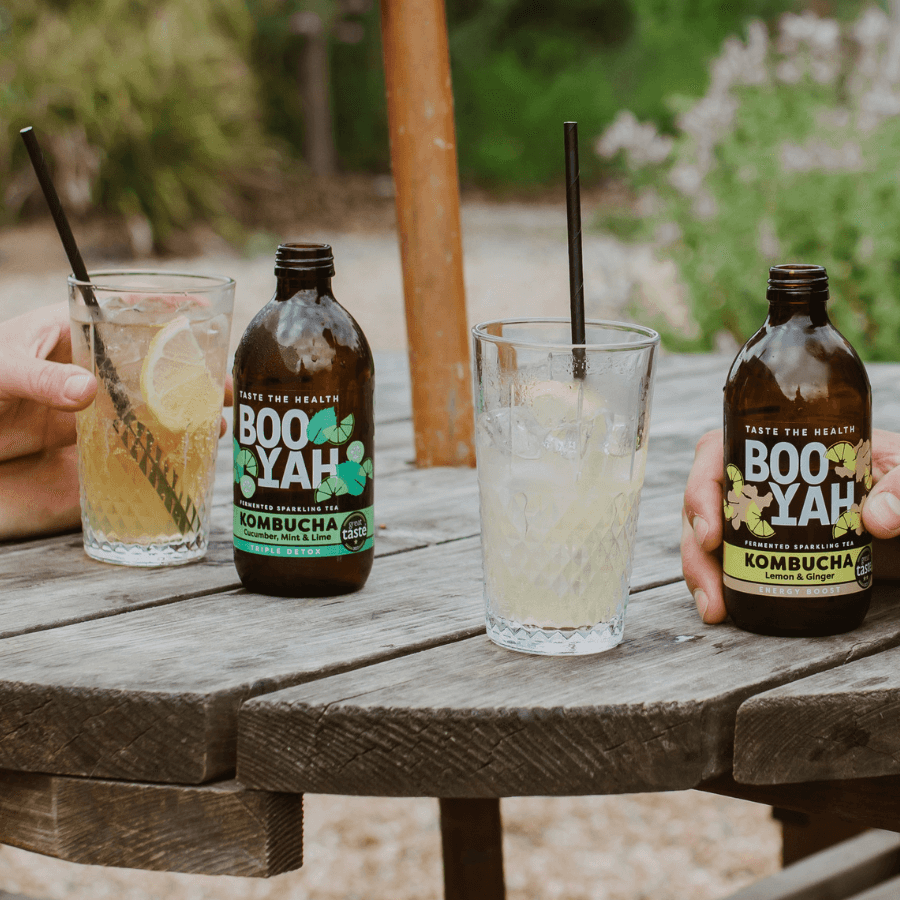 Two bottles of Booyah kombucha in glasses on a wooden table outdoors.